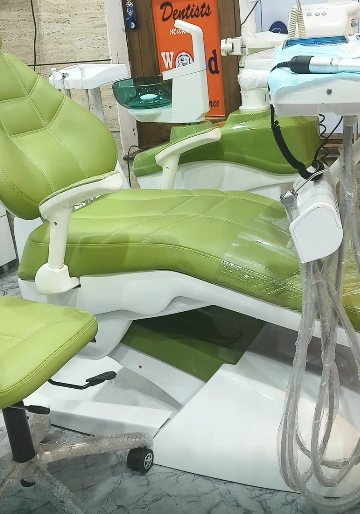 The treatment room at N.K Dental Smile Studio — a green upholstered dental chair with the delivery unit and suction lines beside it
